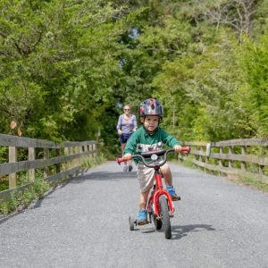 Child cycling with parent walking behind