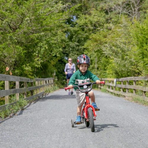 Child cycling with parent walking behind